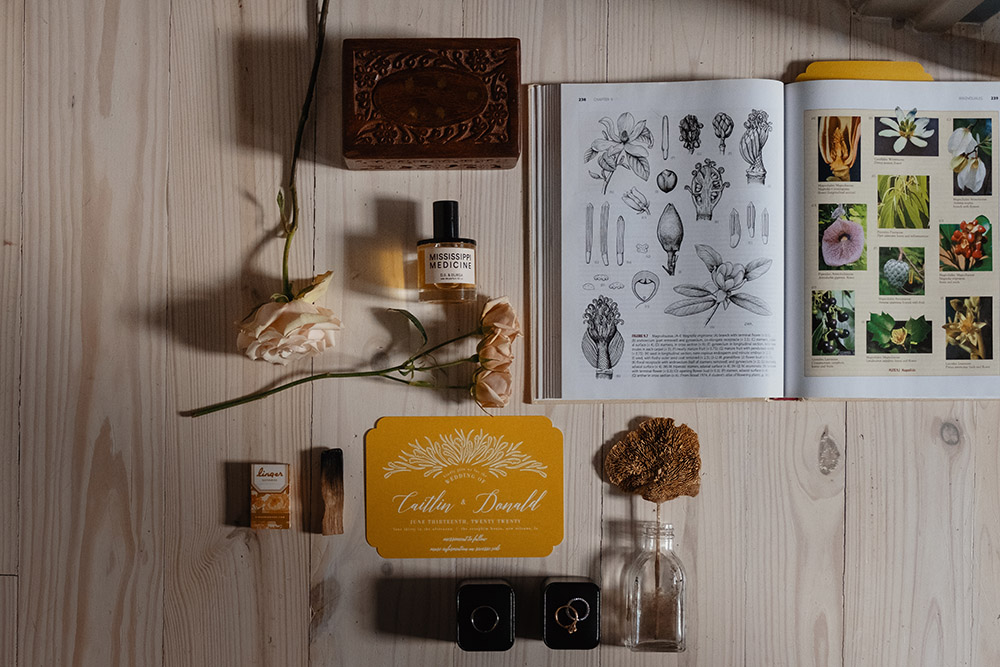 The wedding invitation, rings and a botany book flatlay. Photo: Dark Roux