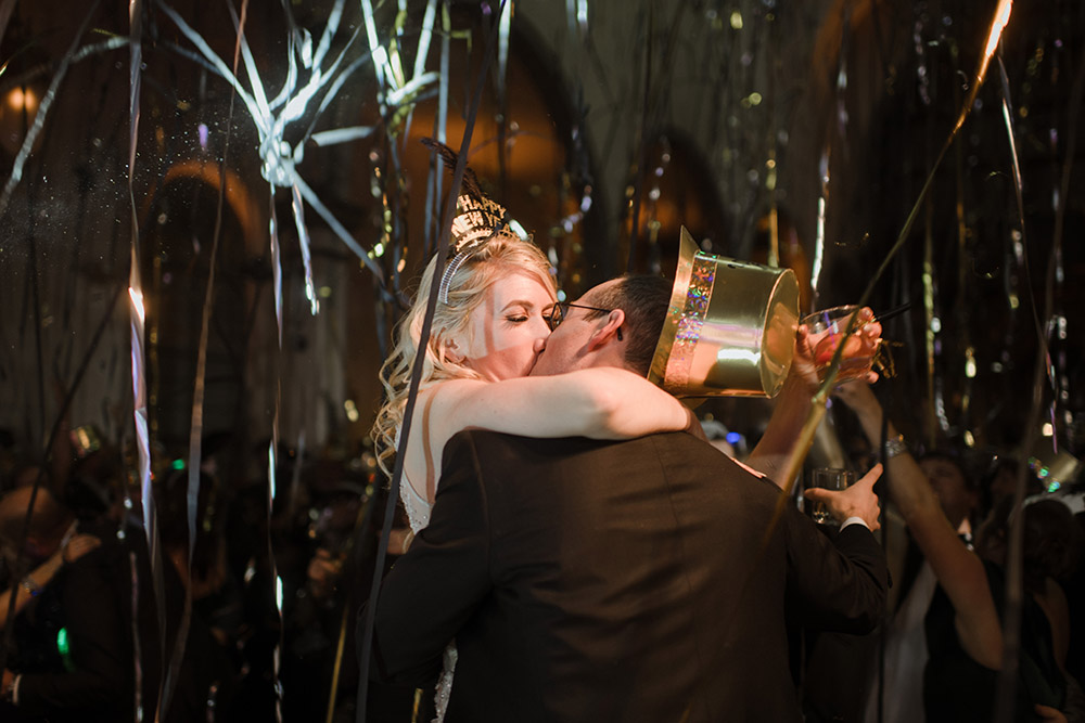The newly weds kiss at midnight as streamers and confetti fall around them.