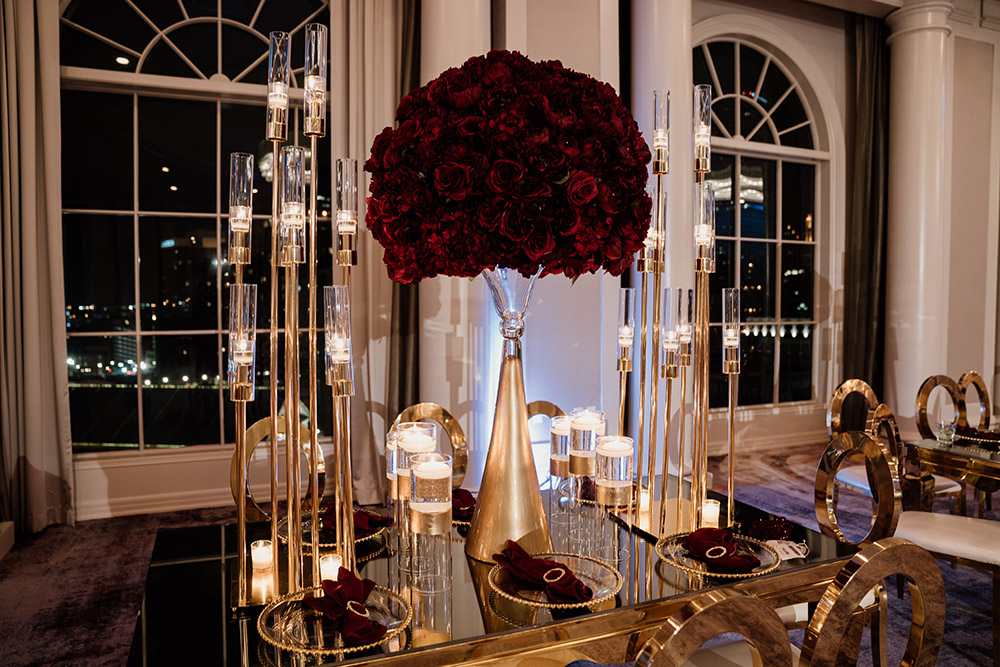 Close up of the gold and glass tables with candles and burgundy rose centerpieces. Photo by Audie Jackson