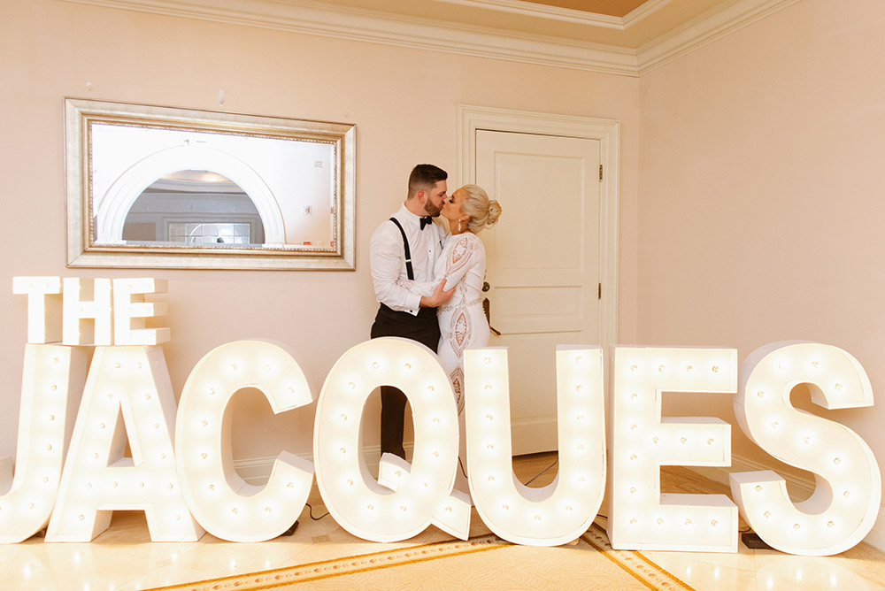 The bride and groom pose with marquee letters spelling their name