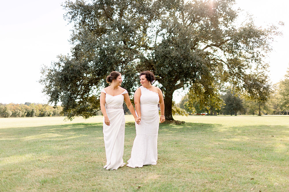the brides hold hands and walk on the grounds of The Barn at Sarah Bella in Picauyne. MS