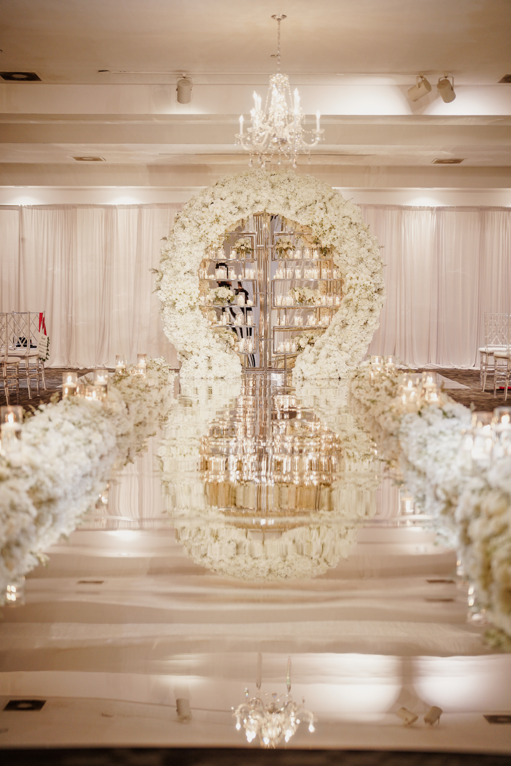 Mirror aisle wedding ceremony with lush white flower arch and candle backdrop