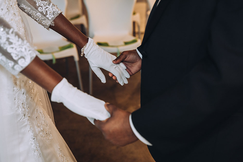 bride wearing white gloves holding groom's hands