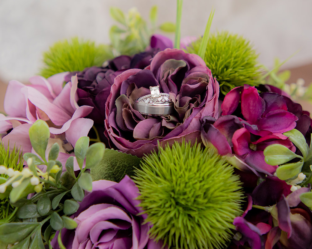purple and green wedding bouquet with wedding rings