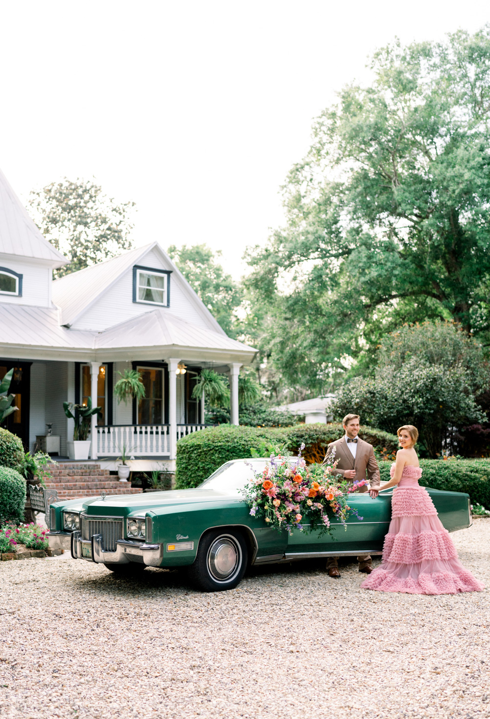 A bride and groom pose by an antique convertible in front of the Henry Smith House.